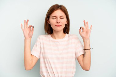 Mavi arka planda izole edilmiş genç İngiliz kadın yoğun bir günün ardından rahatlıyor, yoga yapıyor..