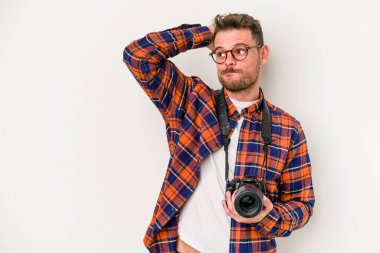 Kafkasyalı genç fotoğrafçı beyaz arka planda izole edilmiş kafasının arkasına dokunuyor, düşünüyor ve bir seçim yapıyor..