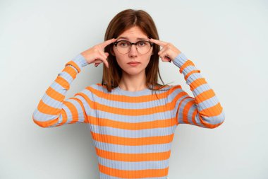 Mavi arka planda izole edilmiş genç bir İngiliz kadın bir göreve odaklanmış, işaret parmaklarını işaret ediyor..