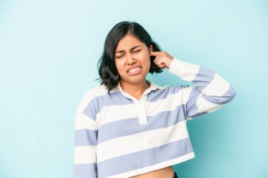 Mavi arka planda izole edilmiş genç Latin kadın kulaklarını elleriyle kapatıyor..
