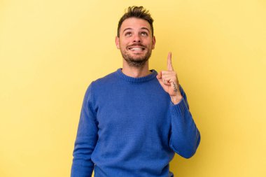 Sarı arka planda izole edilmiş genç beyaz bir adam iki parmağı da boş bir alan gösteriyor..