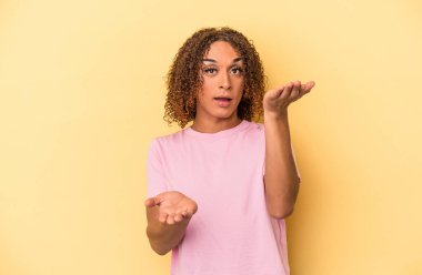 Sarı arka planda izole edilmiş genç Latin transseksüel kadın kollarıyla ölçek oluşturuyor, mutlu ve kendinden emin hissediyor..