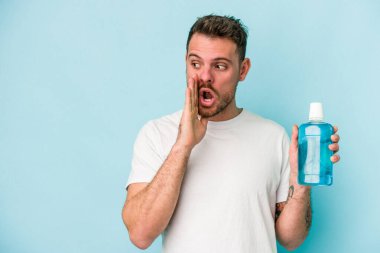 Mavi arka planda ağız gargarası tutan genç beyaz bir adam gizli bir sıcak fren haberi veriyor ve yan bakıyor.