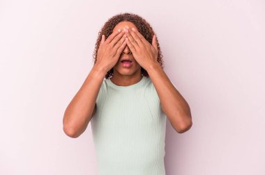 Pembe arka planda izole edilmiş genç Latin transseksüel kadın elleriyle gözlerini kapatmaktan korkuyor..