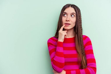 Yeşil arka planda izole edilmiş genç beyaz kadın şüpheli ve şüpheci bir ifadeyle yana bakıyor..