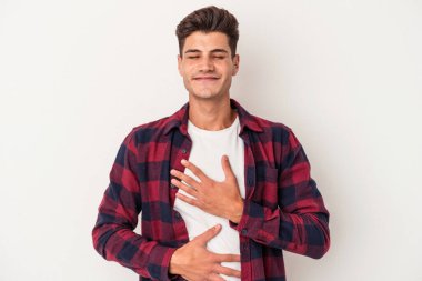 Beyaz arka planda izole genç beyaz adam mutlu bir şekilde gülüyor ve ellerini karnının üstünde tutarak eğleniyor..