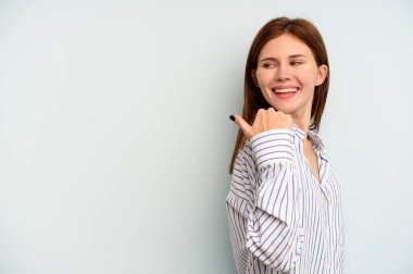 Genç İngiliz kadın mavi arka planda izole edilmiş başparmak uzakta, gülüyor ve kaygısız.