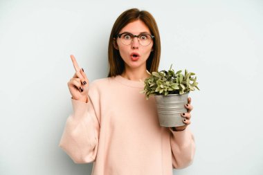 Mavi arka planda izole edilmiş bir bitkiyi tutan genç bir İngiliz kadının harika bir fikri var, yaratıcılık kavramı..