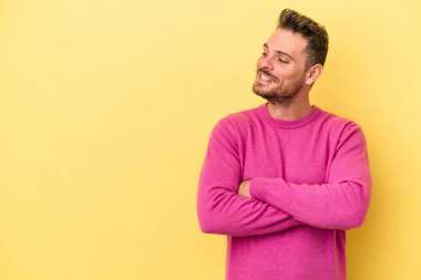 Sarı arka planda izole edilmiş genç beyaz adam kollarını kavuşturarak gülümsüyor..