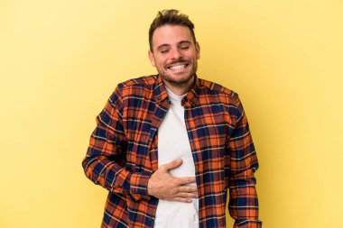 Sarı arka planda izole edilmiş genç beyaz adam karnına dokunur, nazikçe gülümser, yemek yer ve tatmin olur..