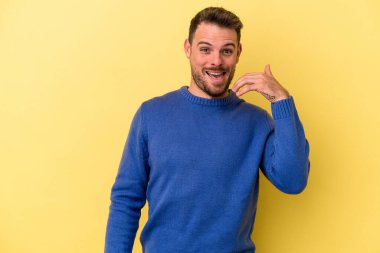 Sarı arka planda izole edilmiş genç beyaz bir adam bir şeye gülüyor, ağızlarını ellerle kapatıyor..