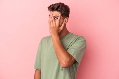 Pembe arka planda izole edilmiş genç beyaz adam kameraya parmaklarıyla göz kırpıyor, yüzünü kapatmaktan utanıyor..