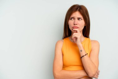 Mavi arka planda izole edilmiş genç bir İngiliz kadın şüpheli ve şüpheci bir ifadeyle yana bakıyor..