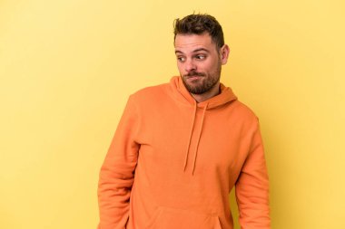 Sarı arka planda izole edilmiş genç beyaz adam omuzlarını silkeliyor ve gözleri açık..