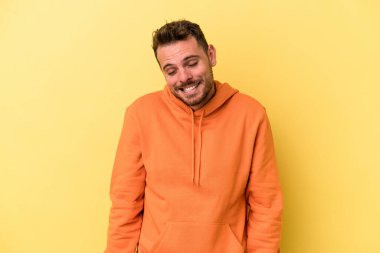 Sarı arka planda izole edilmiş genç beyaz adam gülüyor ve gözlerini kapıyor, rahatlamış ve mutlu hissediyor..