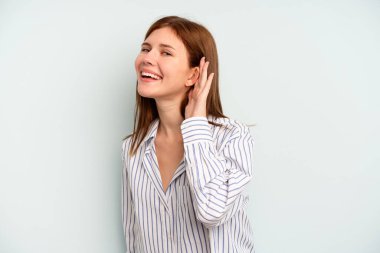 Genç İngiliz kadın mavi arka planda izole edilmiş bir şekilde bir dedikoduyu dinlemeye çalışıyor..