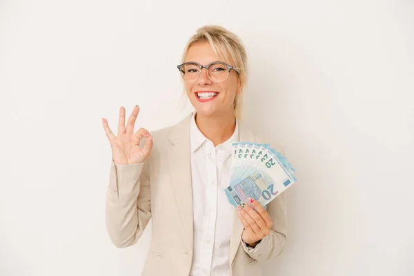 若いビジネスロシアの女性は 白の背景に明るく自信を持って孤立した銀行券を保持Okジェスチャーを示す — ストック写真