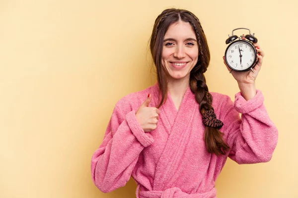 Jovem Caucasiana Vestindo Roupão Banho Segurando Despertador Isolado Fundo Amarelo — Fotografia de Stock