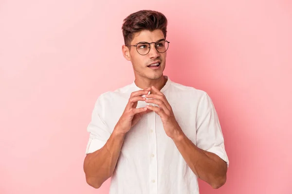 Young caucasian man isolated on pink background making up plan in mind, setting up an idea.