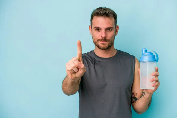Młody Biały Mężczyzna Pije Milkshake Odizolowany Niebieskim Tle Pokazując Numer — Zdjęcie stockowe