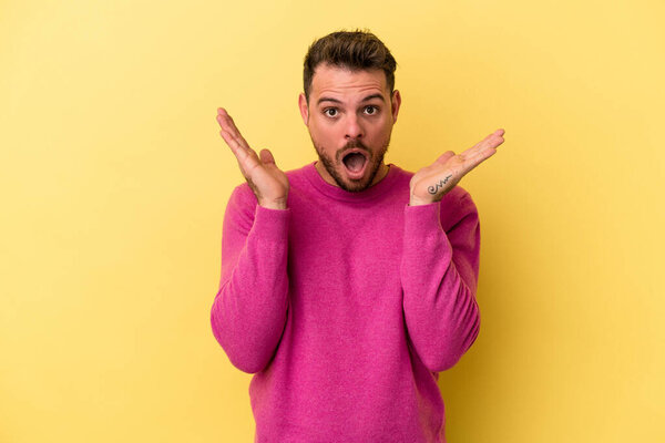 Молодой кавказский человек на желтом фоне удивлен и шокирован.