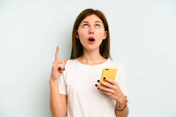 Молодая Английская Женщина Держит Мобильный Телефон Изолирован Синем Фоне Указывая — стоковое фото