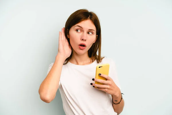 Młoda Angielka Trzymająca Telefon Komórkowy Niebieskim Tle Próbująca Słuchać Plotek — Zdjęcie stockowe