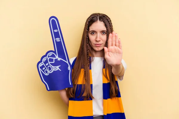 Young sports fan woman isolated on yellow background standing with outstretched hand showing stop sign, preventing you.