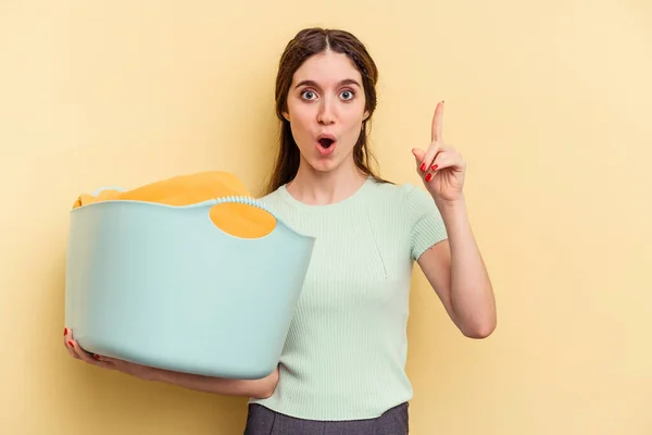 Young Caucasian Woman Holding Clothes Basket Isolated Yellow Background Having — Stock Photo, Image