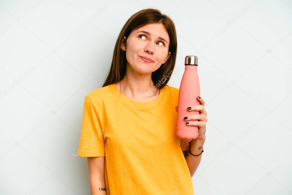 Young English woman holding a thermo isolated on blue background dreaming of achieving goals and purposes