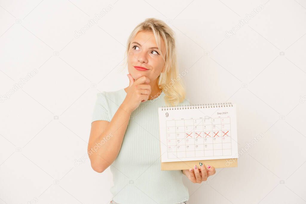 Young Russian woman holding a calendar isolated on white background looking sideways with doubtful and skeptical expression.