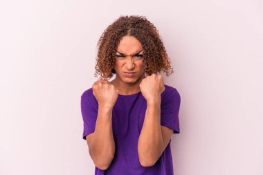 Pembe arka planda izole edilmiş genç Latin transseksüel kadın yumruğunu kameraya gösteriyor, agresif yüz ifadesi..