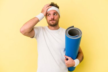 Sarı arka planda izole edilmiş bir minderi tutarken yoga derslerine giden beyaz bir genç şoka uğruyor..