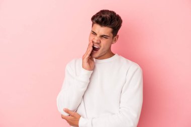 Pembe arka planda izole edilmiş genç beyaz adam esniyor. Ağzı eliyle kapatan yorgun bir hareket sergiliyor..