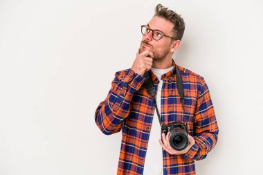 Beyaz arka planda izole edilmiş genç beyaz fotoğrafçı şüpheli ve şüpheci bir ifadeyle yana bakıyor..