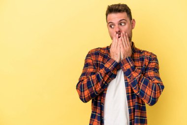 Kafkasyalı genç adam sarı arka planda izole edilmiş. Düşünceli bir şekilde, ağzını eliyle kapatan bir fotokopi odasına bakıyor..