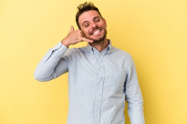 Sarı arka planda izole edilmiş genç beyaz adam parmaklarıyla bir cep telefonu hareketi gösteriyor..