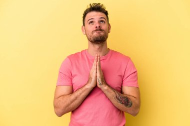 Sarı arka planda izole edilmiş genç beyaz bir adam el ele tutuşup ağız kenarında dua ediyor, kendinden emin hissediyor..