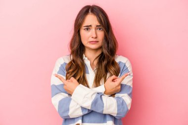 Pembe arka plan noktalarında izole edilmiş genç beyaz kadın iki seçenek arasında seçim yapmaya çalışıyor..