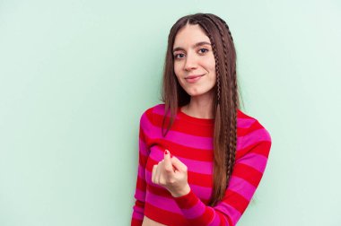 Yeşil arka planda izole edilmiş genç beyaz kadın sanki seni davet ediyormuş gibi seni işaret ediyor..