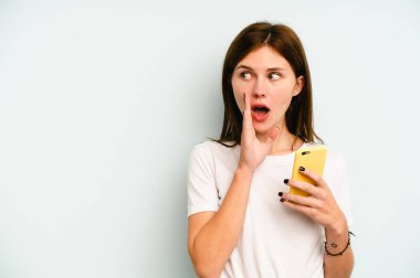 Mavi arka planda cep telefonu tutan genç İngiliz kadın gizli bir sıcak fren haberi veriyor ve yana bakıyor.