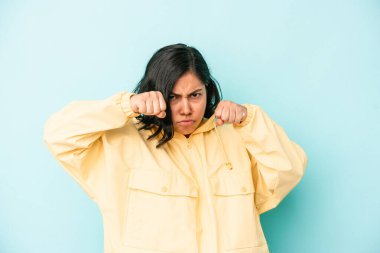 Mavi arka planda izole edilmiş genç Latin bir kadın bir tartışma yüzünden yumruk, öfke, kavga atıyor, boks yapıyor..