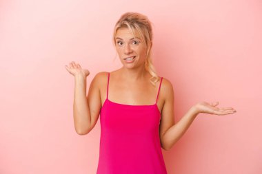 Pembe arka planda izole edilmiş genç bir Rus kadın. Kafası karışmış ve omuz silkiyor..
