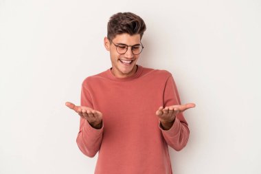 Beyaz arka planda izole edilmiş genç beyaz bir adam elinde avuç içi bir şeyle kameraya sunuyor..