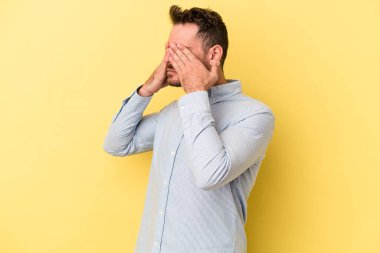 Sarı arka planda izole edilmiş genç beyaz adam elleriyle gözlerini kapatmaktan korkuyor..