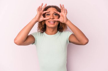 Pembe arka planda izole edilmiş genç Latin transseksüel kadın bir başarı fırsatı bulmak için gözlerini açık tutuyor..