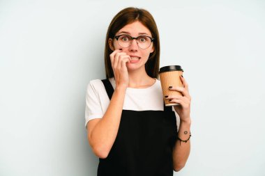 Restoran garsonu elinde kahve tutan kadın mavi arka planda izole edilmiş tırnak yiyor, gergin ve endişeli..