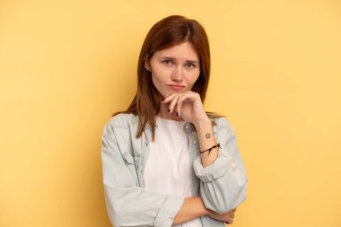 Genç İngiliz kadın sarı arka planda izole edilmiş düşünüyor ve yukarı bakıyor, yansıtıyor, düşünüyor, hayal kuruyor..