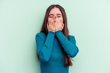 Yeşil arka planda izole edilmiş genç beyaz bir kadın bir şeye gülüyor, elleriyle ağzını kapatıyor..