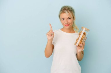 Elinde mavi arka planda izole edilmiş kurabiyeler tutan genç Rus kadın parmaklarıyla bir numarayı gösteriyor..